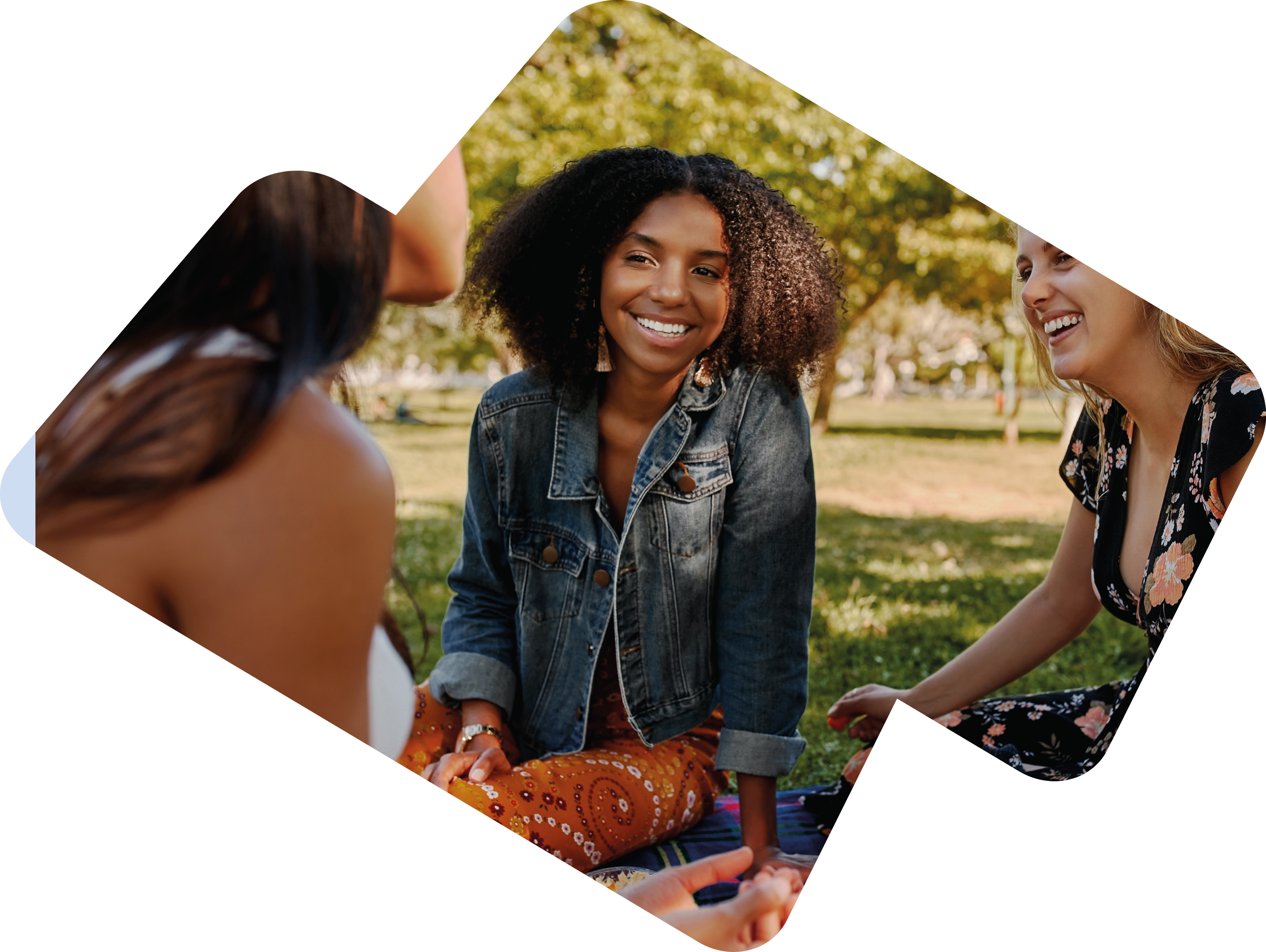 Group of smiling multiracial female best friends sitting together on blanket with fruits enjoying at picnic in the park - group of healthy friends having a picnic